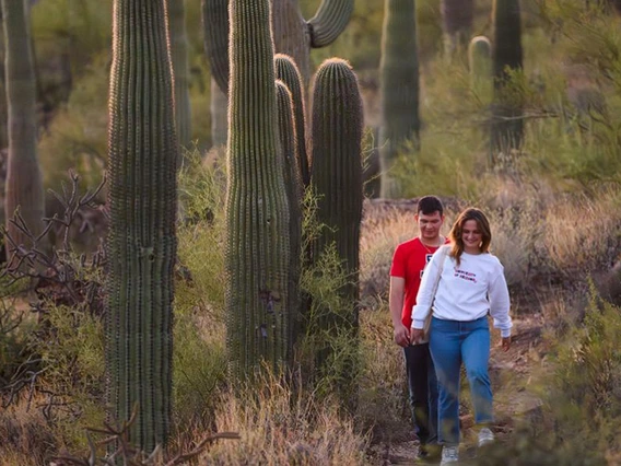 two people walking on trail with saguaro cacti