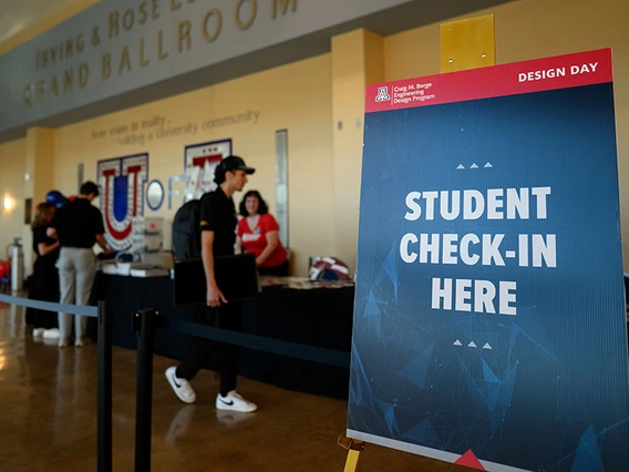 Students sign into the Design Day Open House at a booth in the yellow-toned UA ballroom.