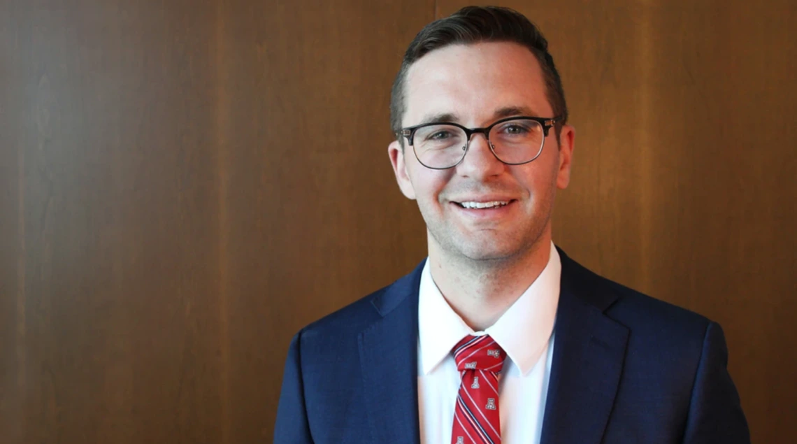 A portrait of a man with brown hair wearing a navy suit jacket and red tie.