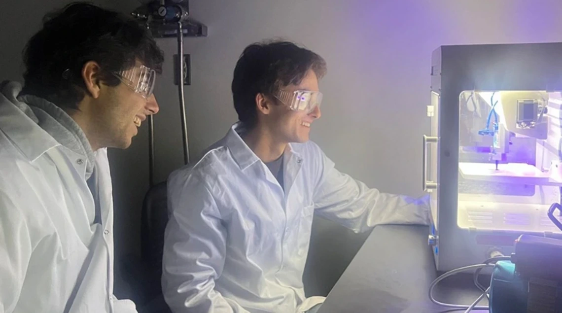 In biomedical engineering assistant professor Shang Song’s lab, undergraduates Ethan Taylor (left) and Lucas Mellinger stand by as a 3D bioprinter creates living cells.