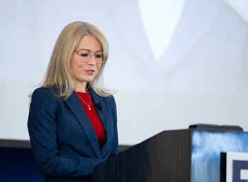 person with long hair, glasses and blue suit at podium